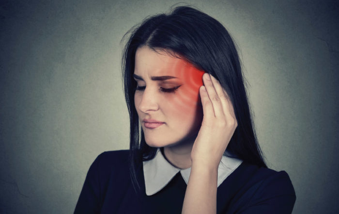 Woman holding the side of her head near her ear, illustrating symptoms associated with tinnitus and ear discomfort.