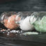 Glass jars filled with Himalayan pink salt, white sea salt, and green gourmet salt spilling onto a dark wooden surface.