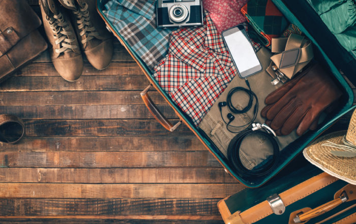 Open suitcase packed with travel essentials including clothing, camera, smartphone, headphones, boots and accessories, ready for a trip.