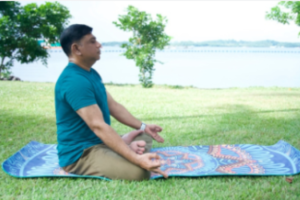 Dr Aneez D.B Ahmed meditating on a yoga mat in a peaceful park setting, practicing mindfulness as part of his daily wellness routine.
