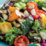 A colourful mixed vegetable salad with cherry tomatoes, leafy greens, and almond slices in a turquoise bowl.