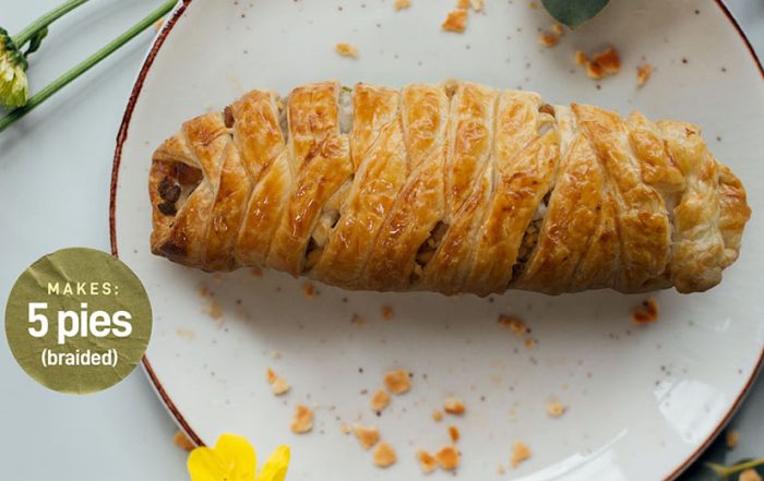 Golden braided Chicken Sausage Pie on a white plate, baked to perfection with flaky puff pastry.