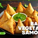 Plate of golden baked vegetable samosas arranged in a circle around a bowl of green mint chutney, featured by Prime Magazine for a healthy snack recipe.