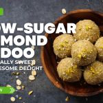 Wooden bowl filled with six low-sugar almond ladoos topped with chopped nuts and coconut flakes, featured by Prime Magazine as a healthy Indian sweet recipe.