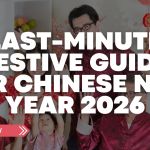 A multi-generation family in Singapore dressed in red celebrating Chinese New Year at home, smiling and raising their hands together in a festive setting.