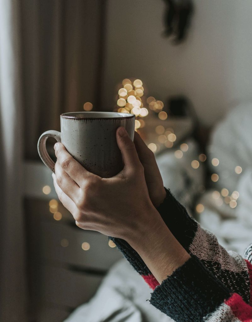 Hands holding a warm mug alone at home during Christmas.