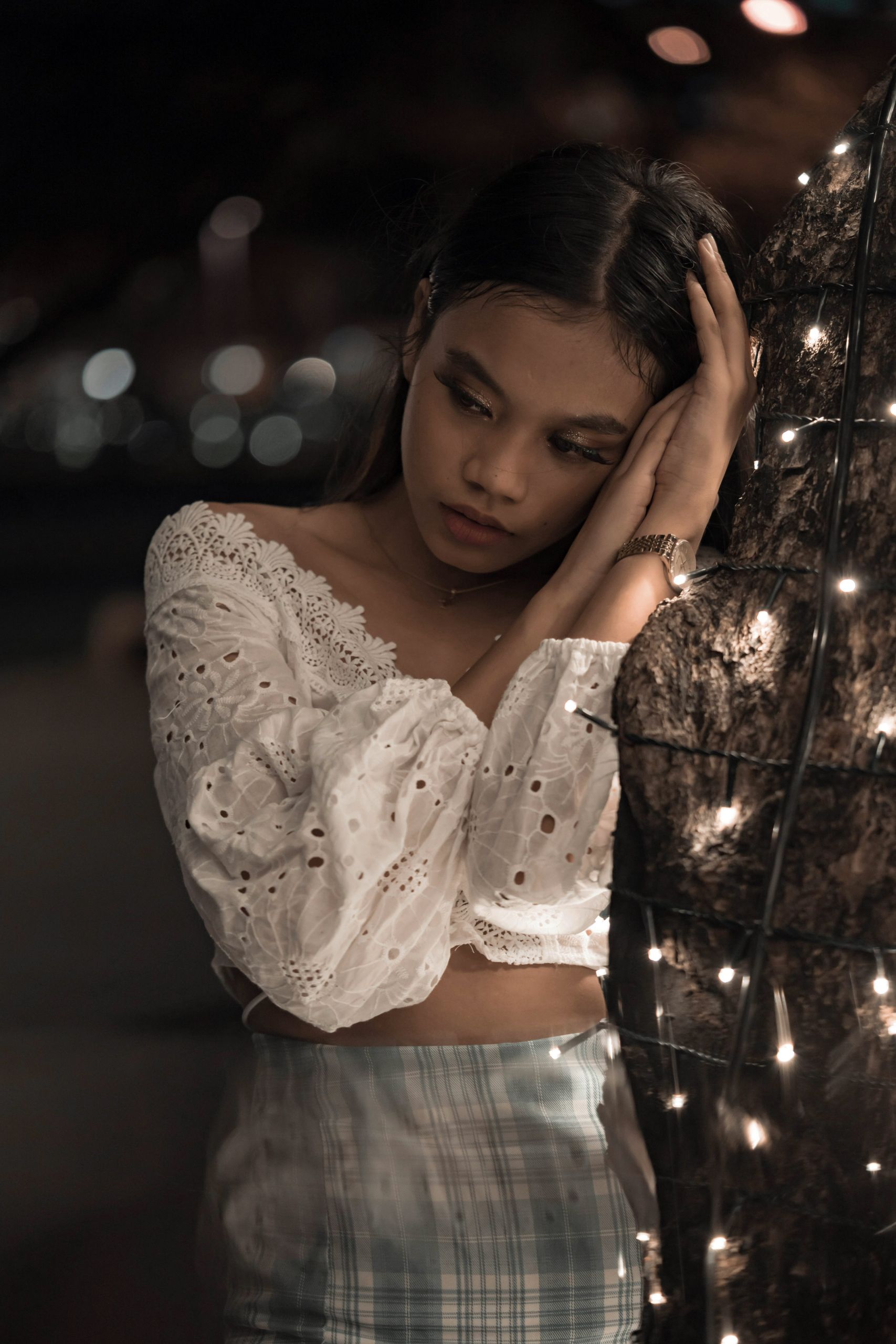 Woman standing alone at night beside glowing holiday lights, expressing loneliness and quiet reflection during Christmas season