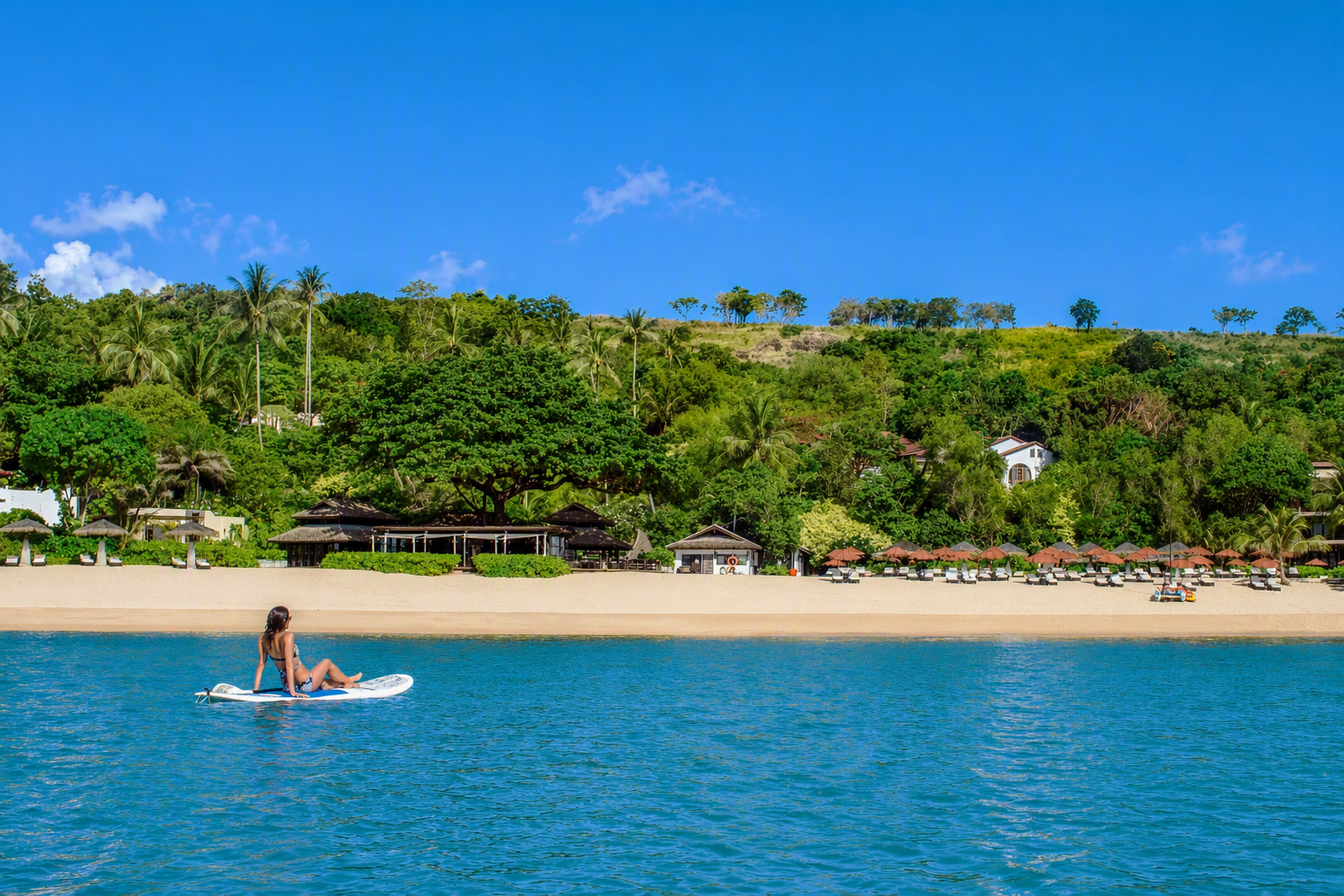 A guest enjoys paddleboarding in the calm waters off the private beach at Garrya Tongsai Bay Samui, surrounded by lush tropical greenery in Koh Samui, Thailand.