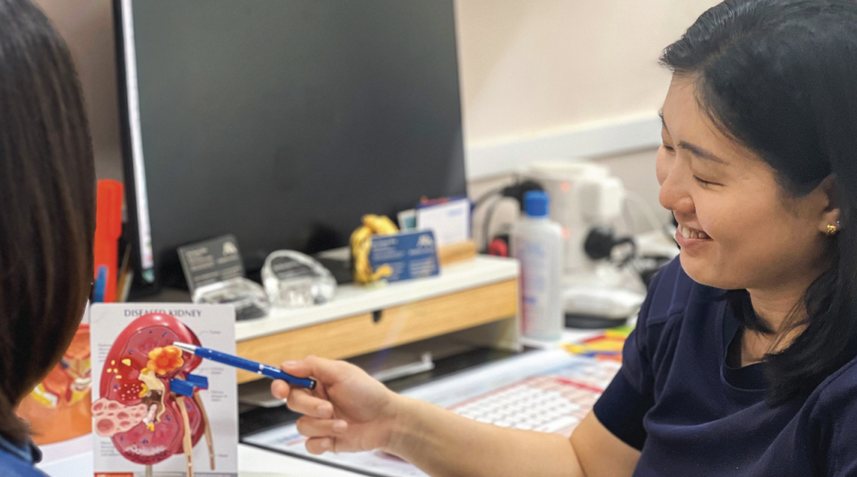 Dr Fiona Wu pointing to an anatomical kidney model with a pen while speaking to a patient.