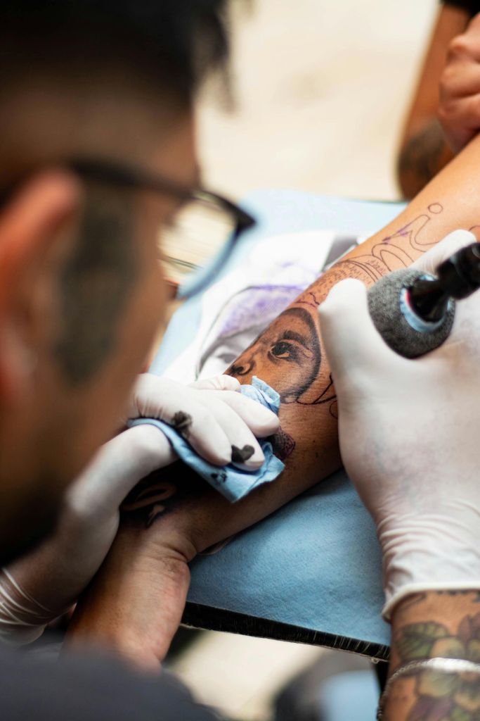 Tattoo artist carefully working on a detailed portrait tattoo, emphasising the importance of choosing an experienced professional for safe body art.